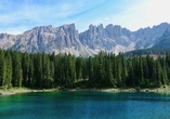 Berge und Bäume spiegeln sich im grünen Karersee in Südtirol.